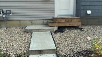 A house with a grey siding exterior, a white front door with the number 7949, and a wooden front step leading to the entrance.