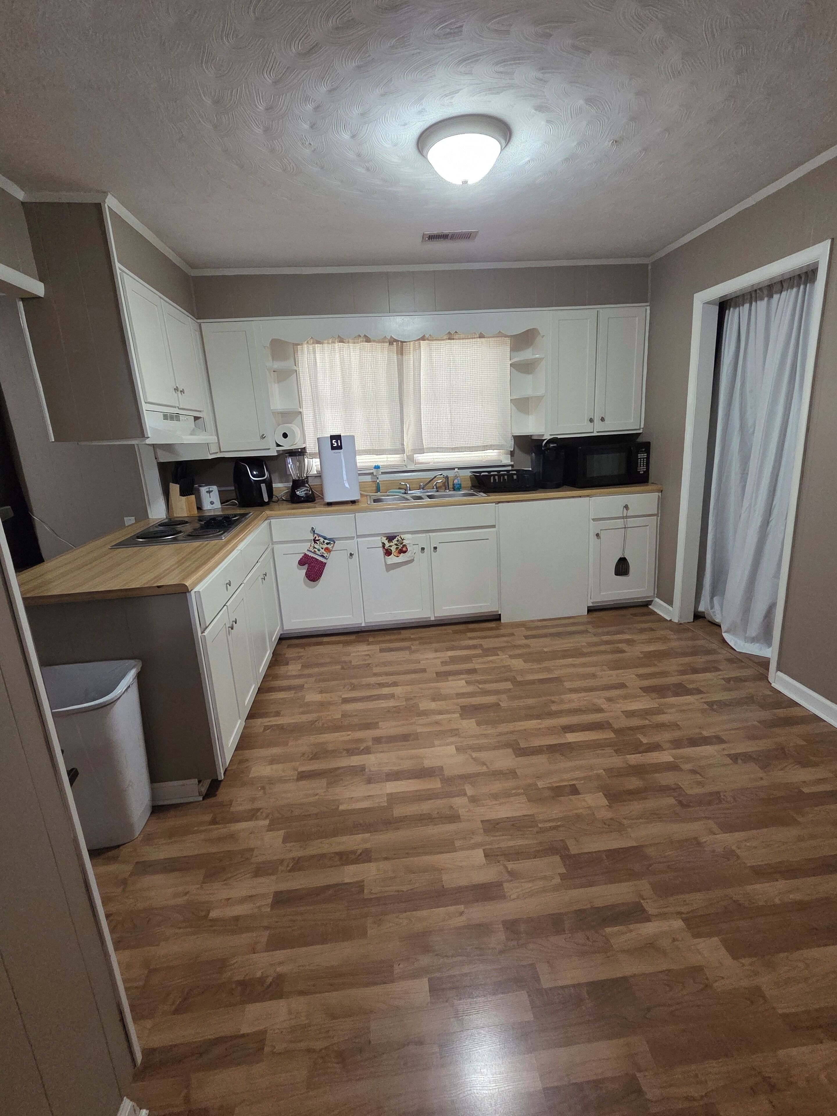 A kitchen with white cabinets, a microwave, a sink, and a window with curtains.