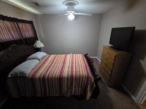 A bedroom with a bed, a dresser, a television, a ceiling fan, and a window with curtains.