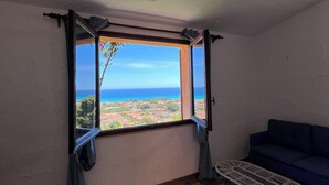 A room with a large window, a blue sofa, and a patterned floor. - Villa Aurea Snow White 139 (Costa Rei)