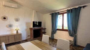 A dining area with a wooden table, white chairs, a TV, and a fireplace. - Villa Aurea Snow White 139 (Costa Rei)