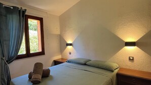 A bedroom with a bed, two bedside tables, a window with curtains, and wall-mounted lights. - Villa Aurea Snow White 139 (Costa Rei)