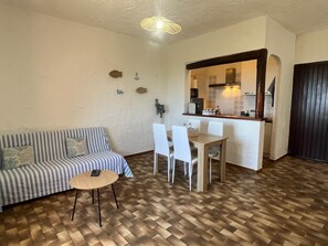 Een woonkamer met een gestreept bankje, een klein rond tafeltje, en een eethoek met een houten tafel en stoelen.