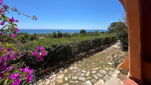 A stone pathway leading to a terrace with a view of the sea and distant landscape.