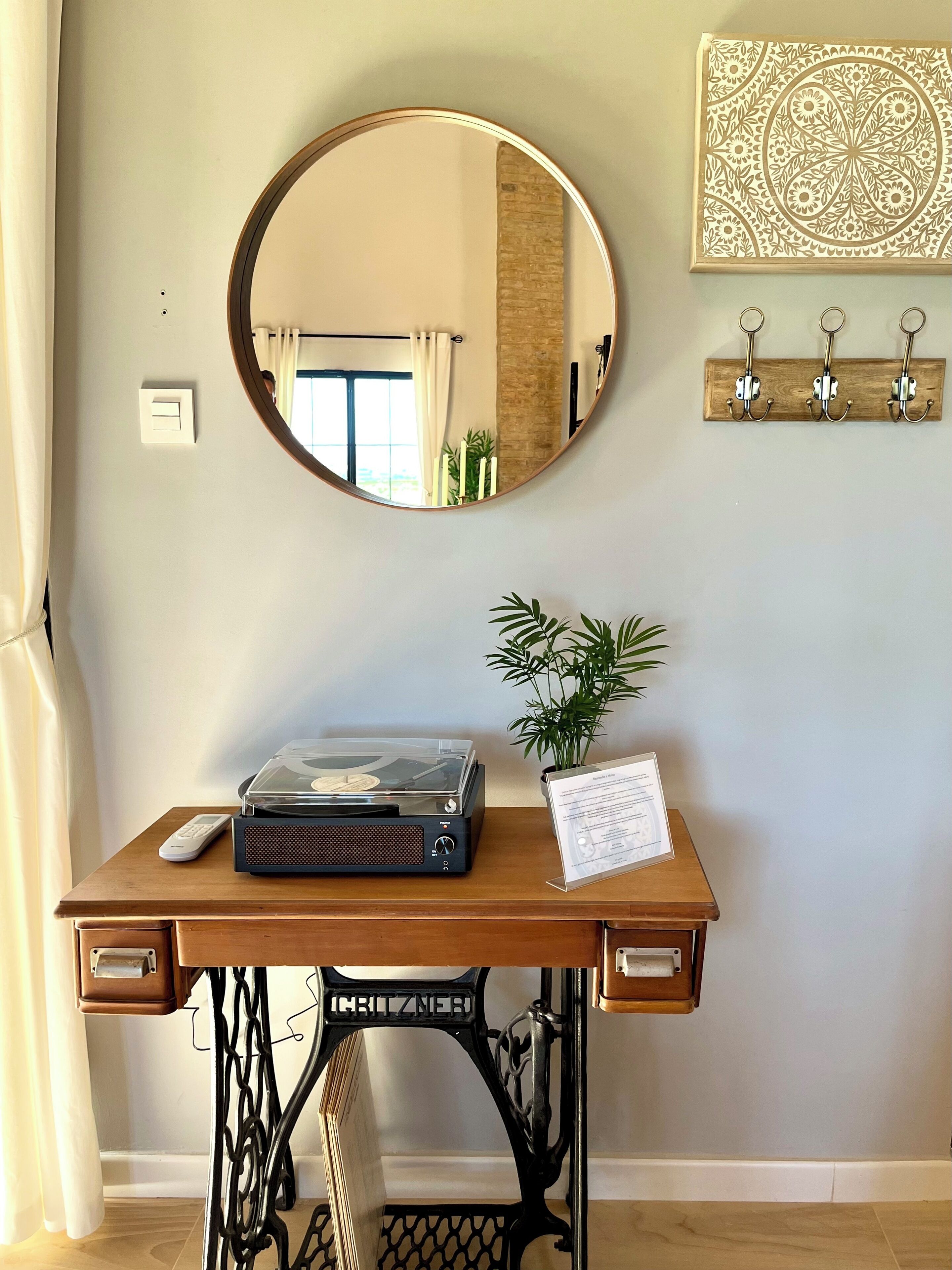 A wooden desk with a vintage sewing machine, a turntable, a remote control, and a potted plant.