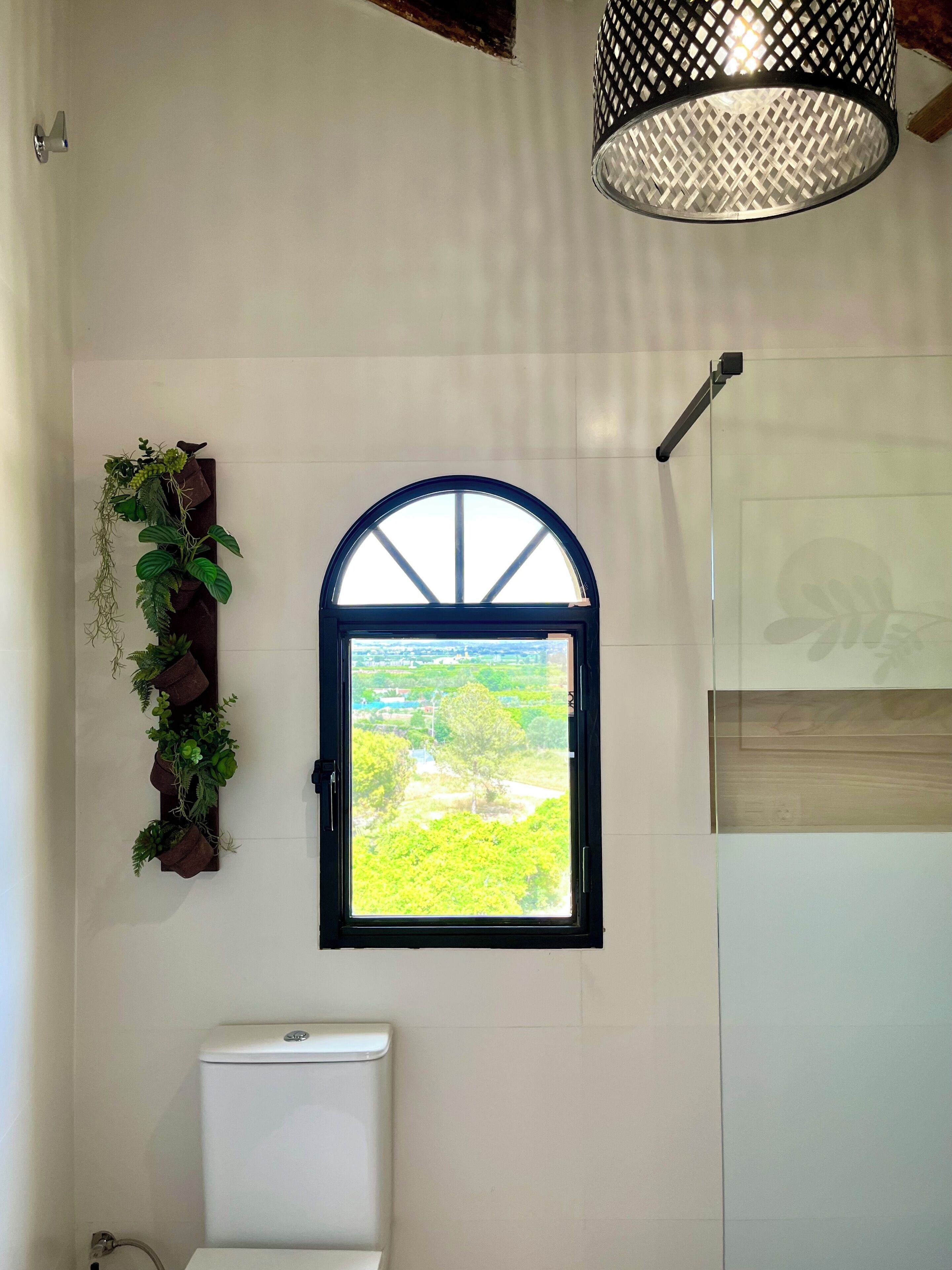 Un baño con ventana, inodoro y planta colgante.