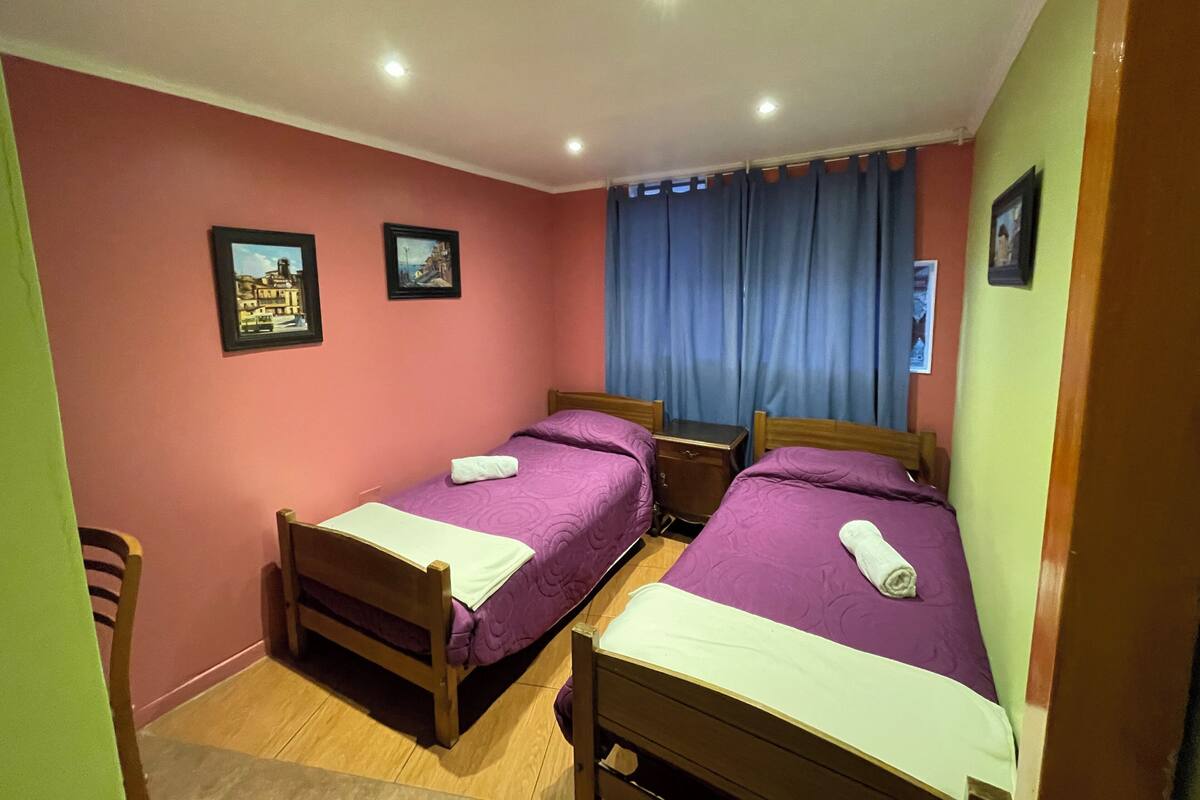 Une chambre avec deux lits, une table de chevet en bois et deux tableaux encadrés au mur.