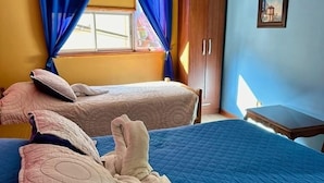 Habitación con dos camas, ropa de cama azul, un armario de madera y un televisor de pantalla plana montado en la pared.
