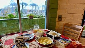 Una mesa de desayuno con mantel floral, una taza de café, huevos revueltos, tostadas y un frutero.