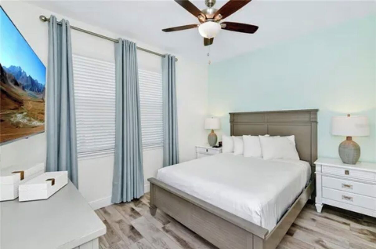 A bedroom with a bed, nightstands, a ceiling fan, and a window with curtains.