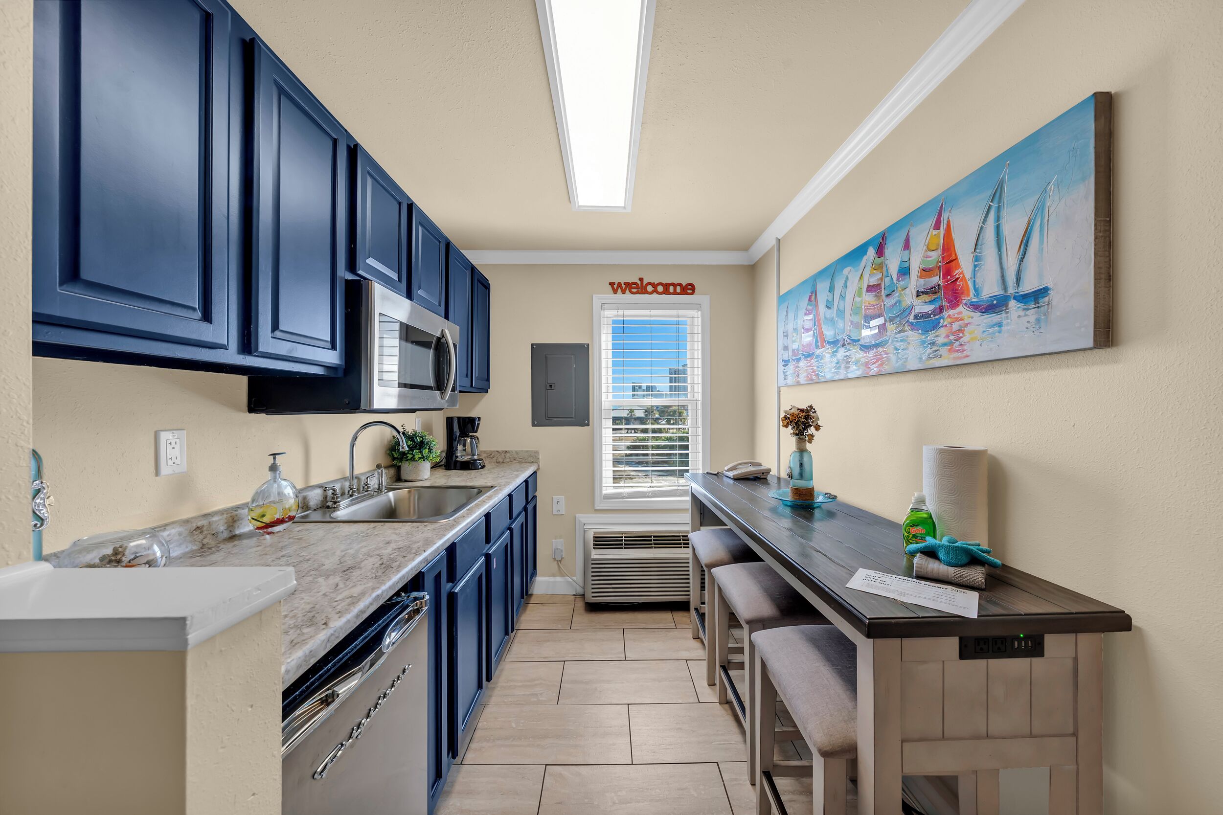 A modern kitchen with dark blue cabinets, a marble countertop, a built-in microwave, and a window with blinds.