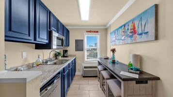 A modern kitchen with dark blue cabinets, a marble countertop, a built-in microwave, and a window with blinds.