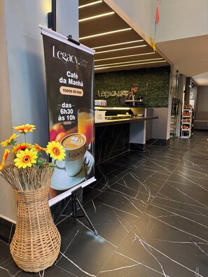 A coffee shop interior with a promotional banner, a counter, and a decorative vase with flowers.