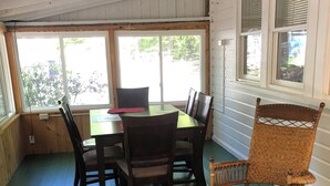 A dining area with a table and chairs, large windows, and a wicker rocking chair.