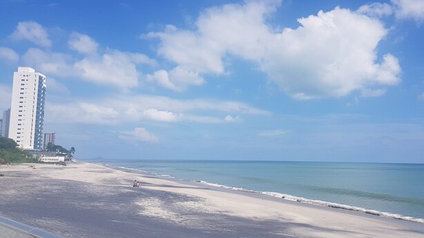 Een strand met een hoog wit gebouw, helderblauwe lucht en een rustige zee.