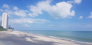 Een strand met een hoog wit gebouw, helderblauwe lucht en een rustige zee.