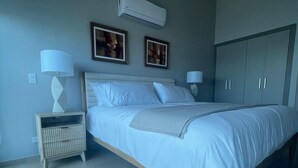 Een moderne slaapkamer met een bed, nachtkastjes, een kledingkast en een airconditioner aan de muur.