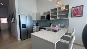 Een moderne keuken met witte kasten, een roestvrijstalen koelkast, een magnetron en een spoelbak. Er hangen hangende lampen en er is een lijst met een foto aan de muur.