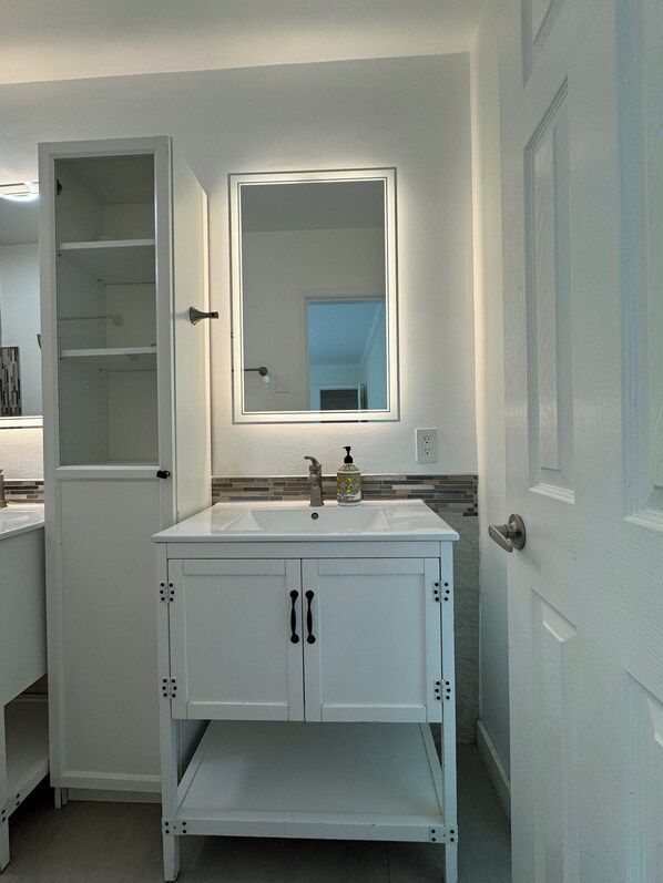 Un baño con tocador blanco, espejo y lavabo.