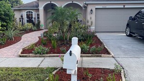 A mailbox in a landscaped garden area with a driveway leading to a house with a garage.