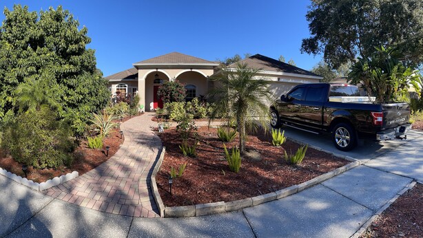 A residential house with a paved driveway, a red door, and a black pickup truck parked in the driveway.