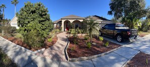 A residential house with a paved driveway, a red door, and a black pickup truck parked in the driveway.