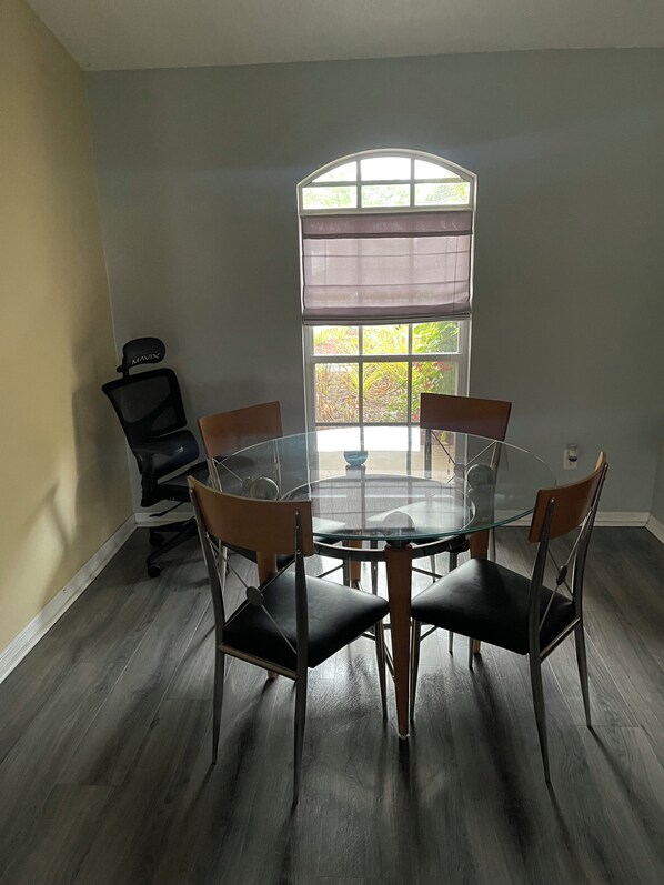 A conference room with a round glass table, six chairs, a black office chair, and a large window with a view of greenery.