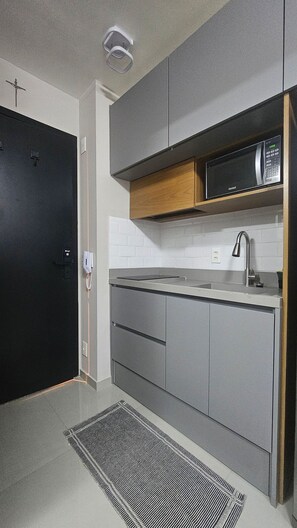 A modern kitchen with grey cabinets, a microwave, and a built-in oven. - Condominio Helbor B.liv (São Paulo)