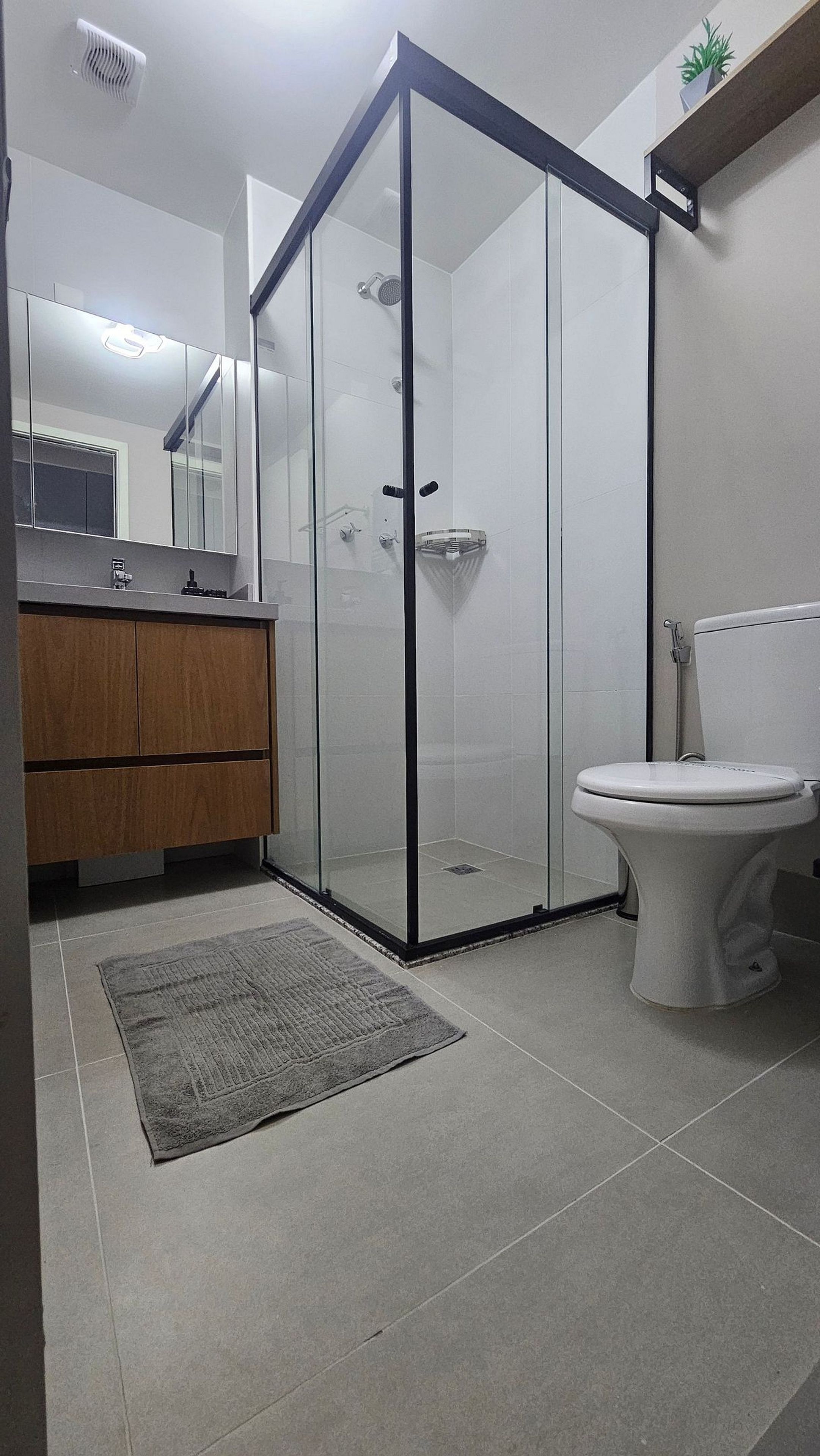 A modern bathroom with a glass shower enclosure, a toilet, and a wooden vanity.