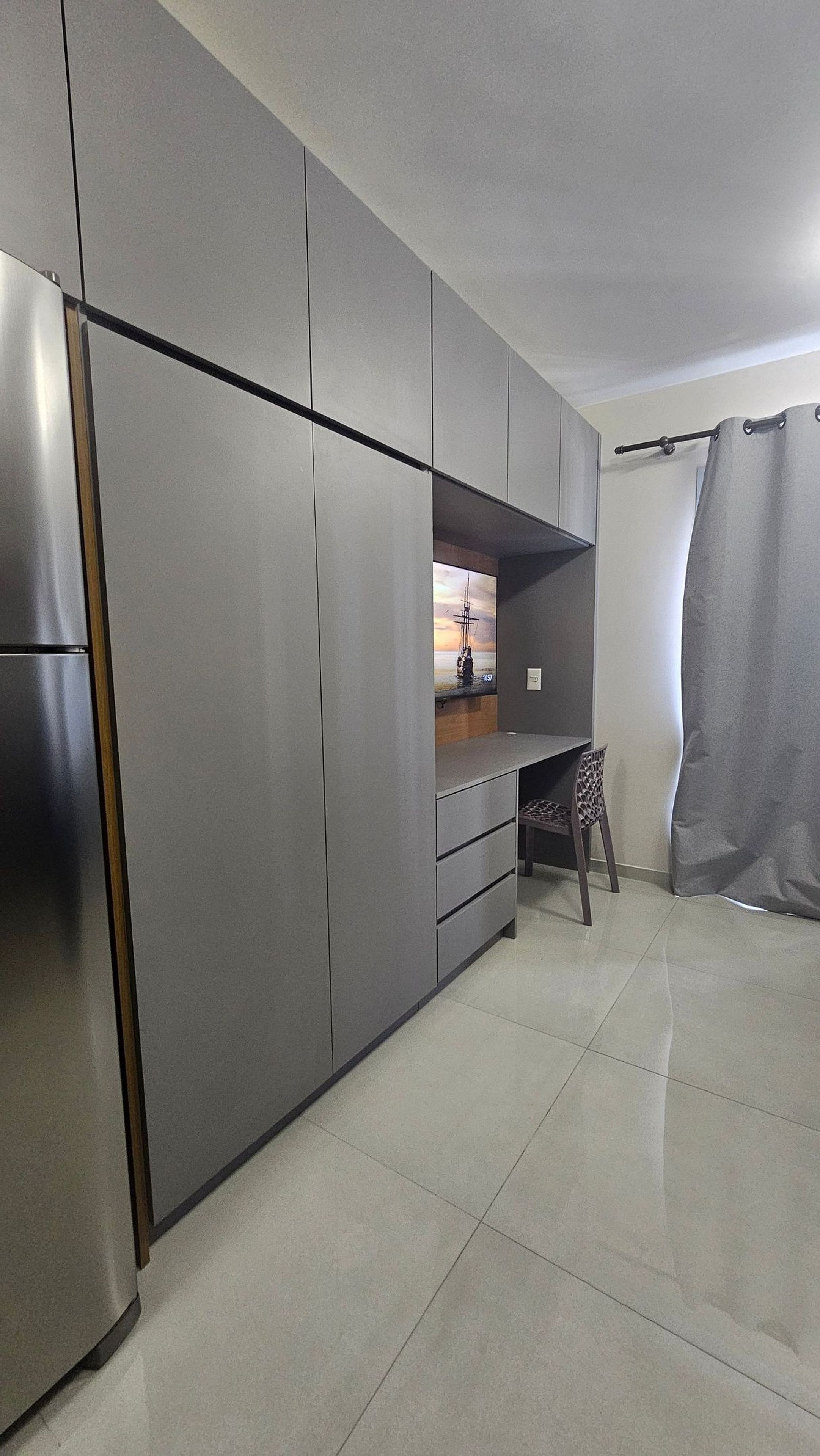 A modern kitchen with a built-in refrigerator, a small seating area with a chair, and a curtain.