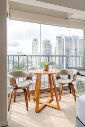 Un apartamento moderno con balcón, dos sillas, una mesa redonda de madera y una planta en maceta.