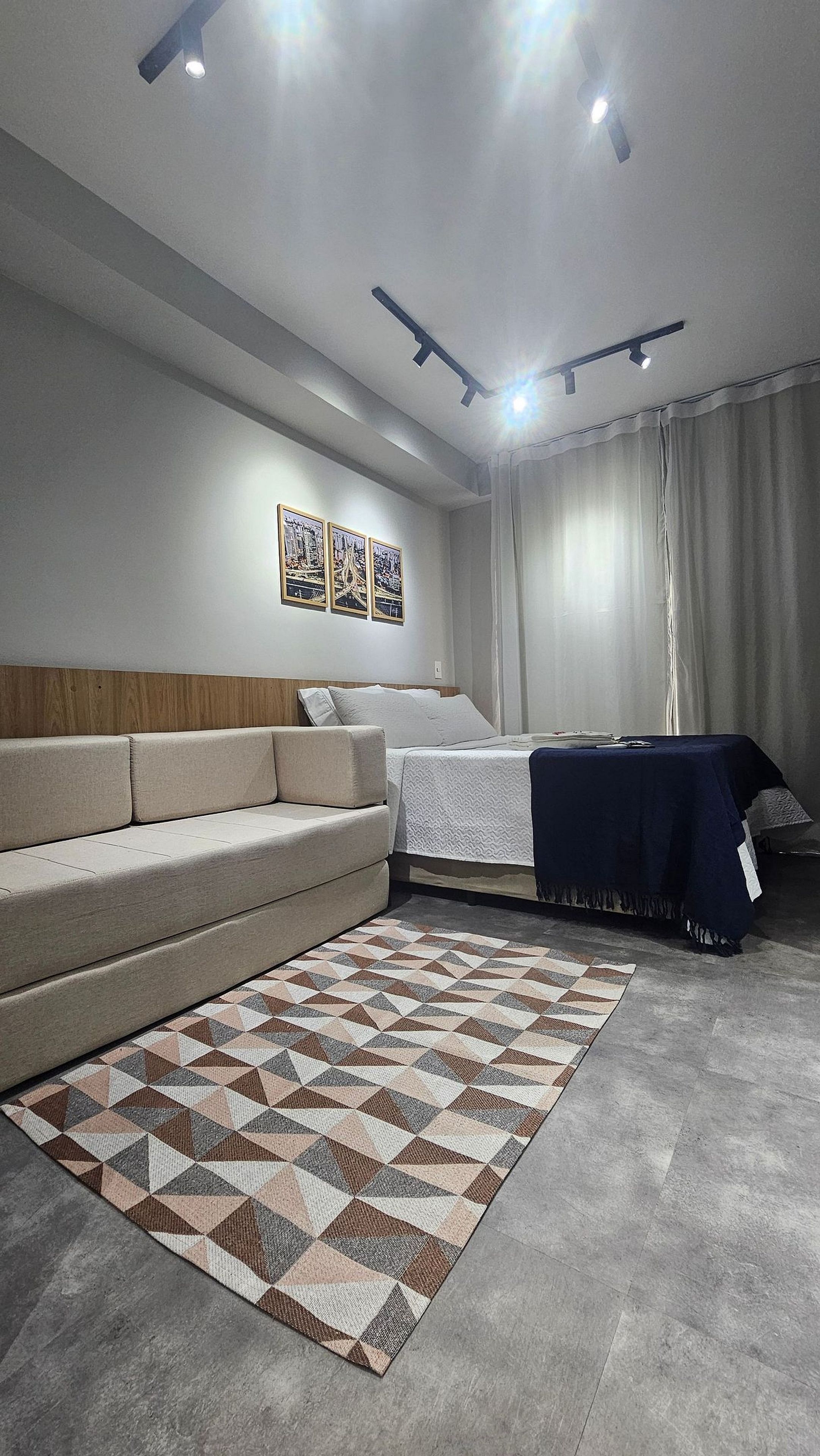 A modern bedroom with a sofa, a bed with a blue cover, a patterned rug, and ceiling lights.