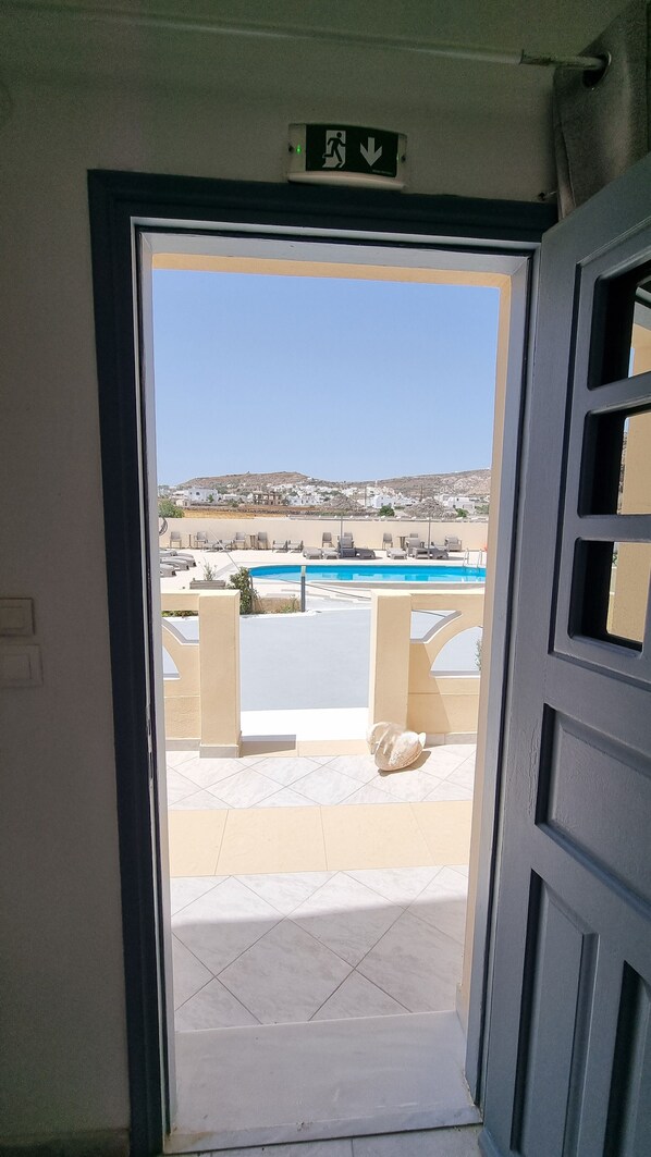 Une porte ouverte donnant sur une terrasse avec une piscine et des chaises longues.