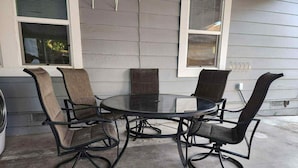 A round glass table with four chairs, each with a high back and a metal frame. The table is set on a concrete floor, and the chairs are positioned around the table. - Studio Near Disney (Santa Ana)