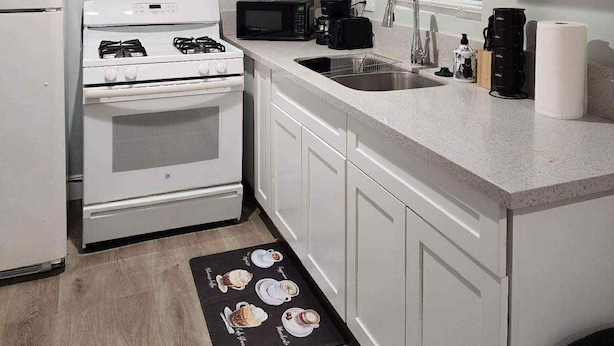 A compact kitchen with white cabinets, a stove, a microwave, and a sink. - Studio Near Disney (Santa Ana)