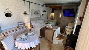 A cozy room with a dining area, a bed with a white headboard, a fireplace, and a television. - A Quiet Corner in the Serra Gaúcha (Picada Café)