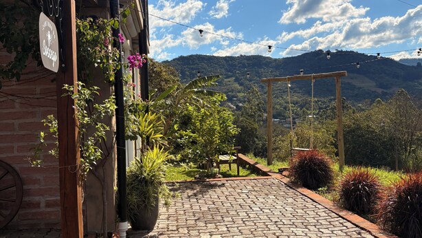A cobblestone pathway leading to a building with a signboard, surrounded by lush greenery and a mountainous backdrop. - A Quiet Corner in the Serra Gaúcha (Picada Café)