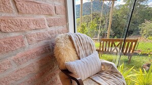 A cozy room with a brick wall, a wooden bench, and a view of a lush garden. - A Quiet Corner in the Serra Gaúcha (Picada Café)