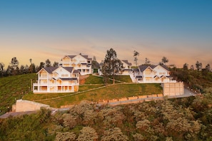 A large, multi-story residential building with multiple balconies, situated on a grassy hillside.