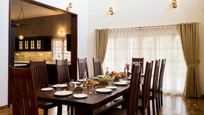 Un comedor con una mesa de madera dispuesta para seis personas, rodeada de sillas. Se ve una cocina a través de un vano abierto, y la habitación tiene una paleta de colores neutra con cortinas color beige.