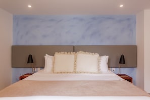 A neatly made bed with a beige blanket, two bedside lamps, and a headboard with a textured design. - Cozy apartment in the historic center of Cartagena de Indias (Cartagena de Indias)