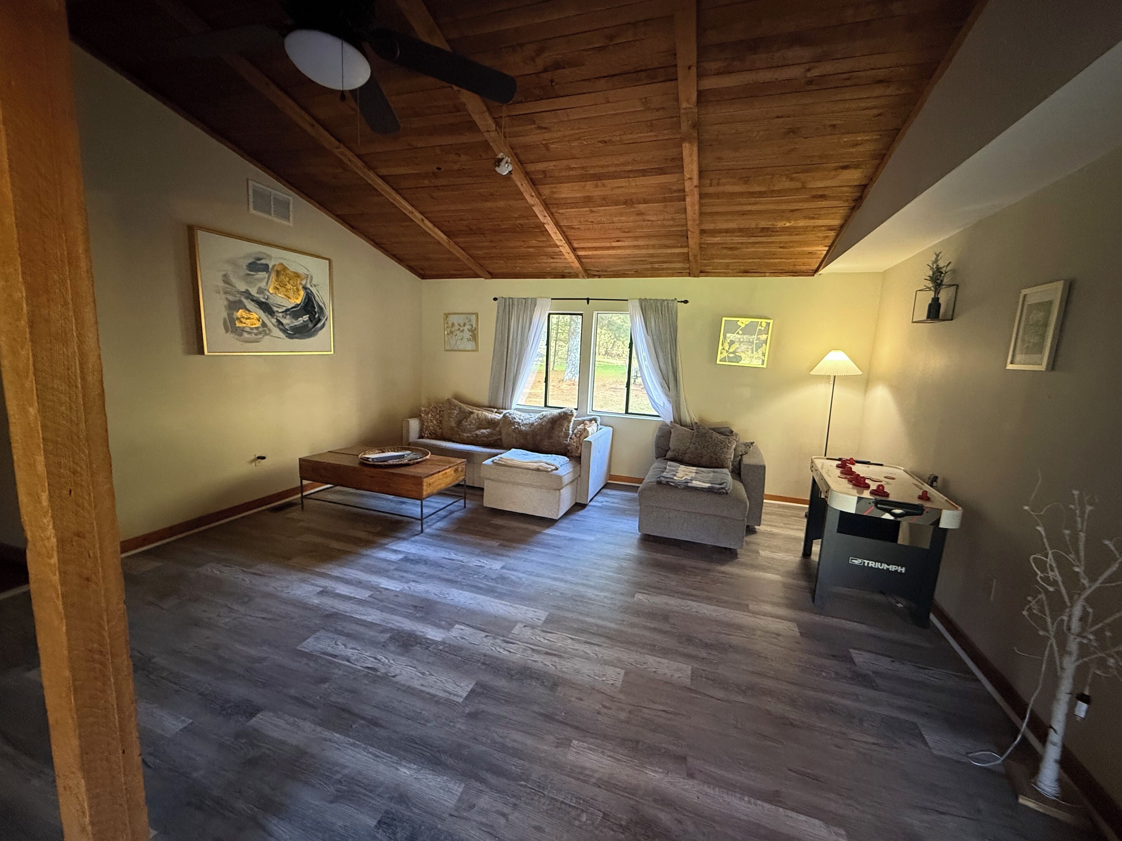 En rummelig stue med træloft, sofa, sofabord og et fodboldbord.
