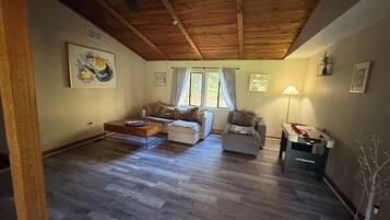 En rummelig stue med træloft, sofa, sofabord og et fodboldbord.