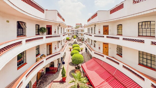 Un patio con edificios blancos, detalles en rojo y un camino central.