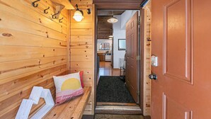 Interior de madera con un banco, una puerta con cerradura electrónica y un pasillo que conduce a una zona de cocina.
