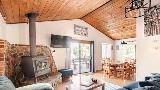 Una sala de estar acogedora con chimenea de piedra, techo de madera y comedor con mesa y sillas.