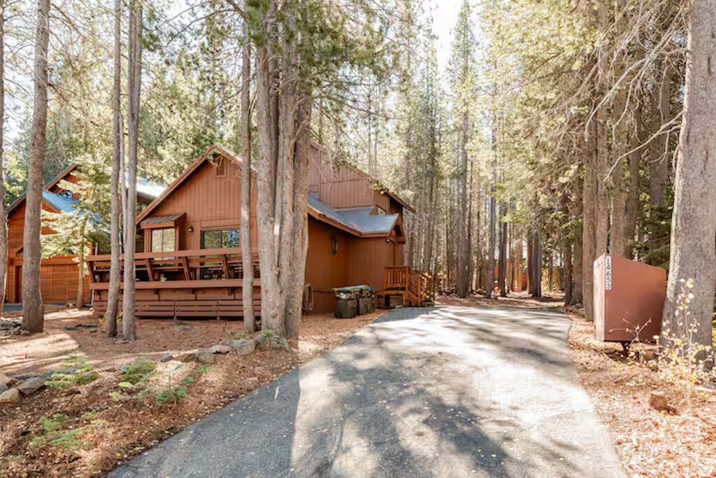 Une cabane aux murs en bois, entourée de grands arbres, et une allée pavée menant à l’entrée.
