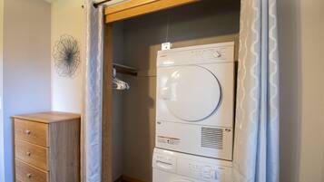 Une petite buanderie équipée d’un lave-linge et d’un sèche-linge superposés, d’un meuble en bois et d’un élément décoratif mural.