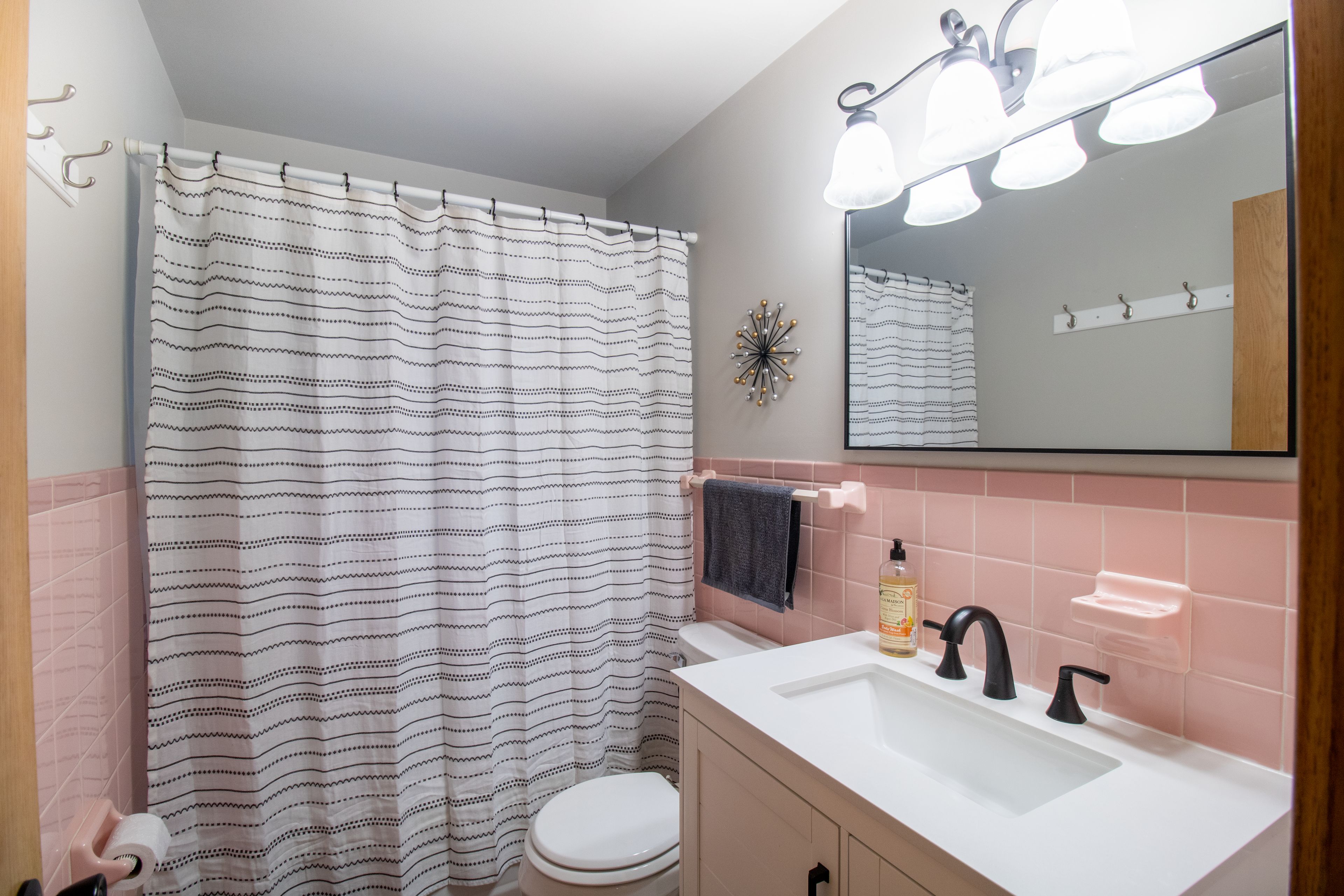 A bathroom with a striped shower curtain, a white toilet, a sink with black faucets, and a mirror above the sink.