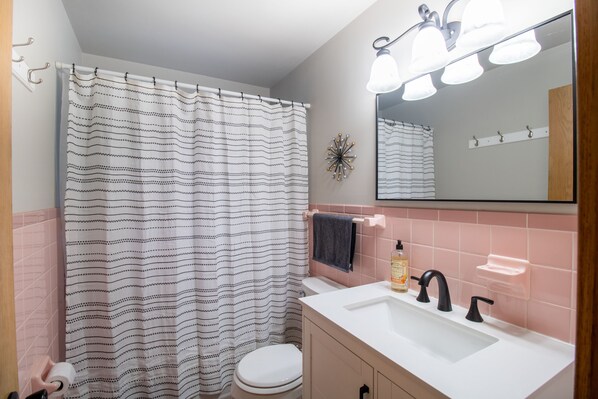 A bathroom with a striped shower curtain, a white toilet, a sink with black faucets, and a mirror above the sink.
